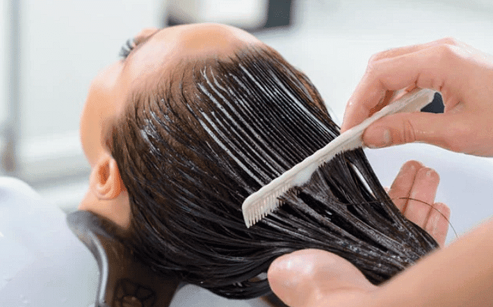 Applying hair conditioner with a comb in a salon setting.