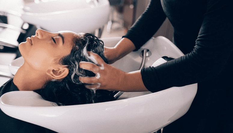 Person getting hair washed at a salon, seen reclining in a sink with a stylist's hands working.