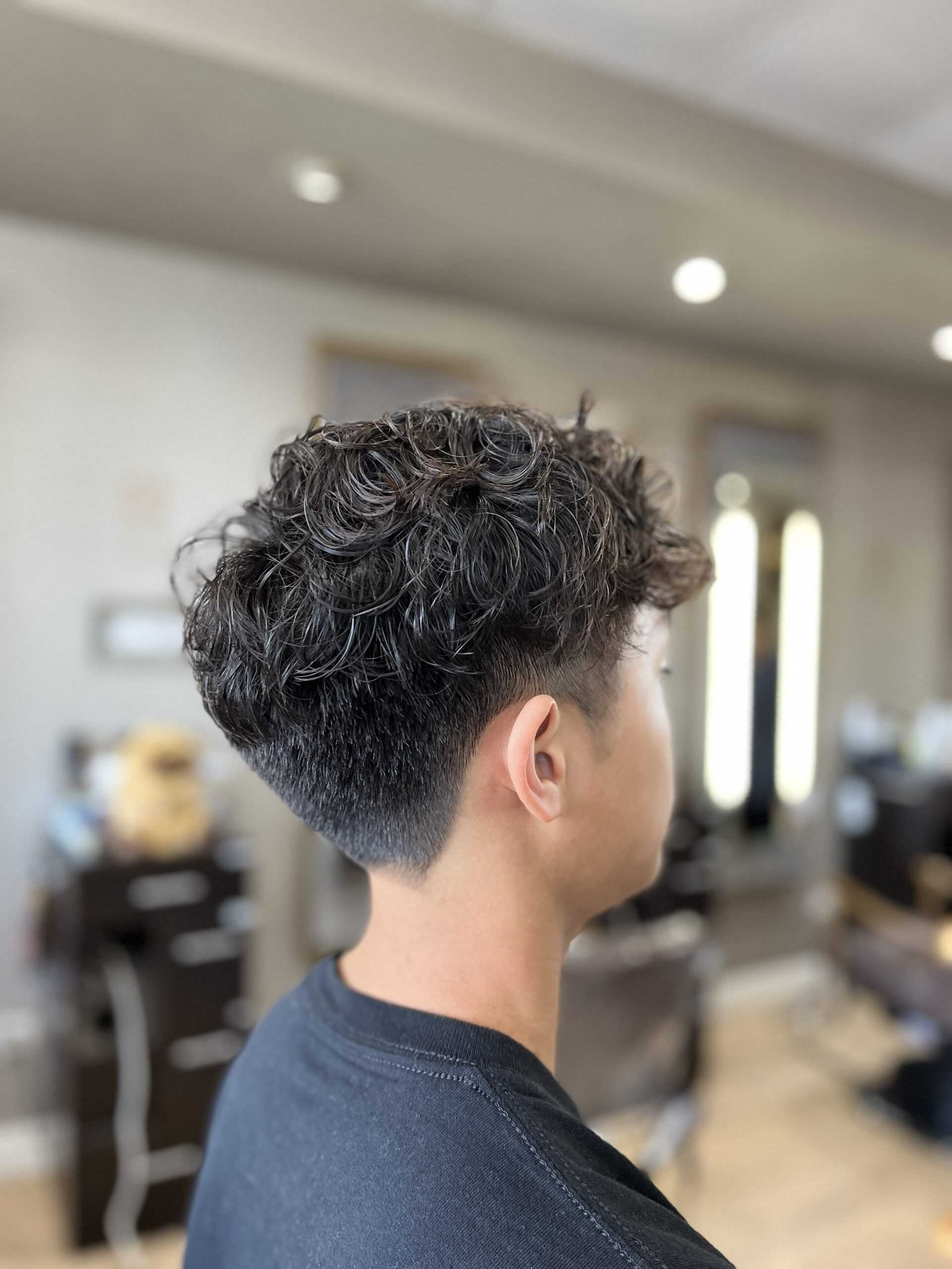 Young man with curly hair and a fresh fade haircut in a modern salon.