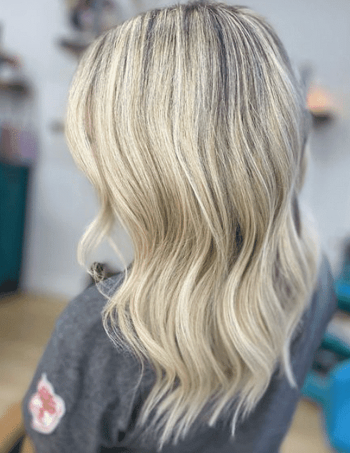 Blonde hair with dark roots styled in loose waves, viewed from the back in a salon setting.