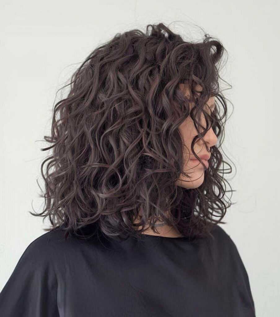Woman with shoulder-length curly hair styled in loose waves, wearing a black top.