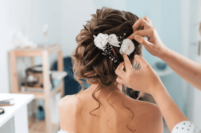 Stylist arranging white flowers in a bride's textured updo.