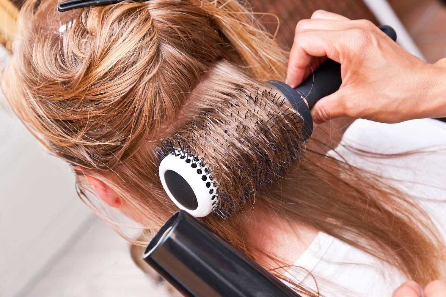 Stylist using a round brush and hairdryer to blow-dry and style a client's hair.