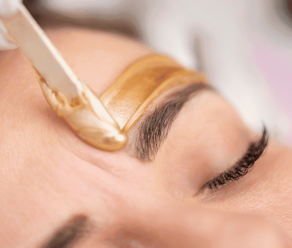Person receiving eyebrow waxing treatment with wax applied to the brow area.