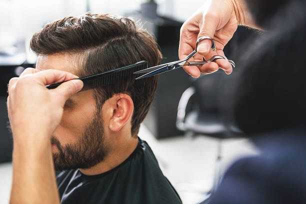 A man getting a haircut in a salon, with scissors and a comb in the stylist's hands.